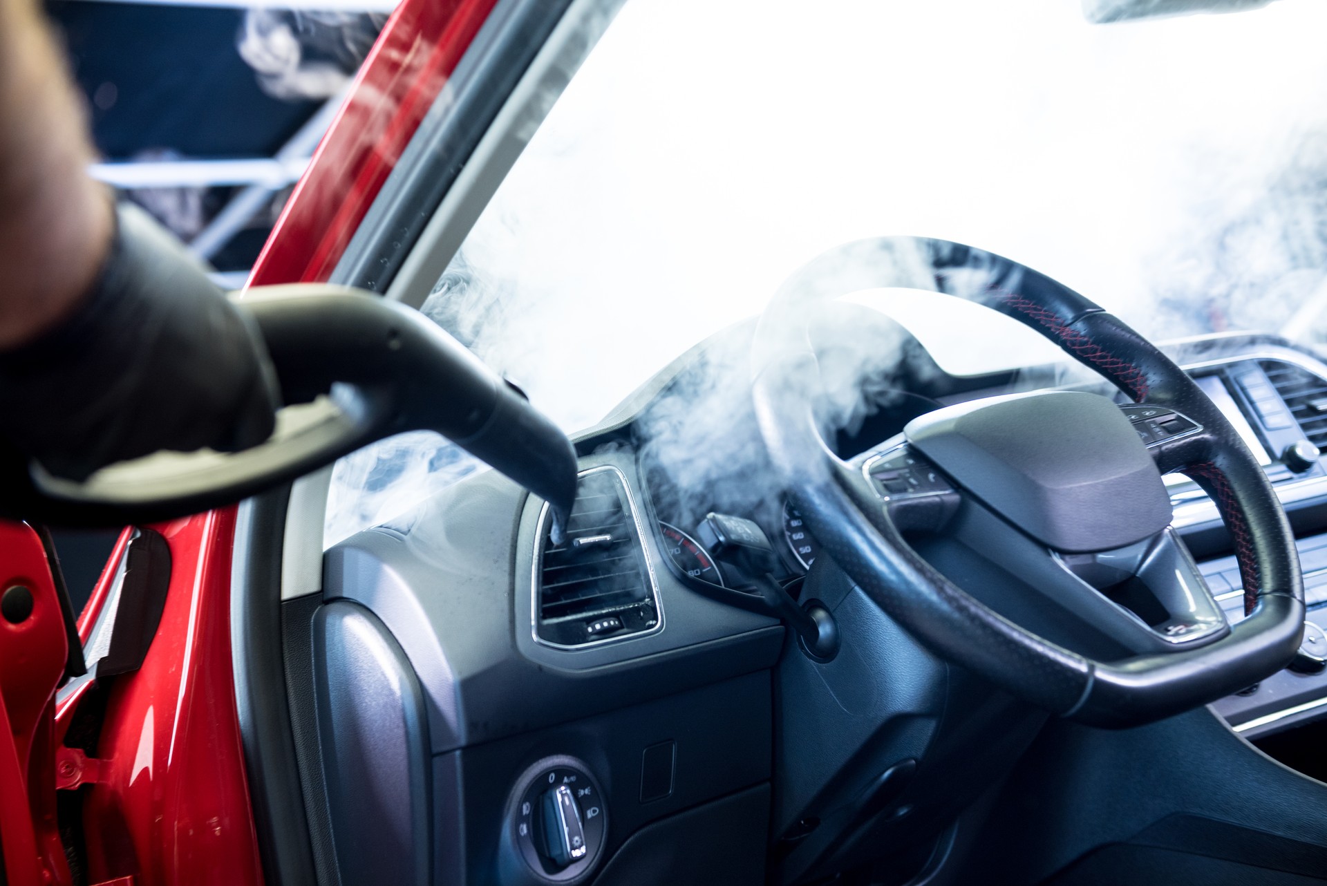 Car service worker cleans interiror with steam cleaner